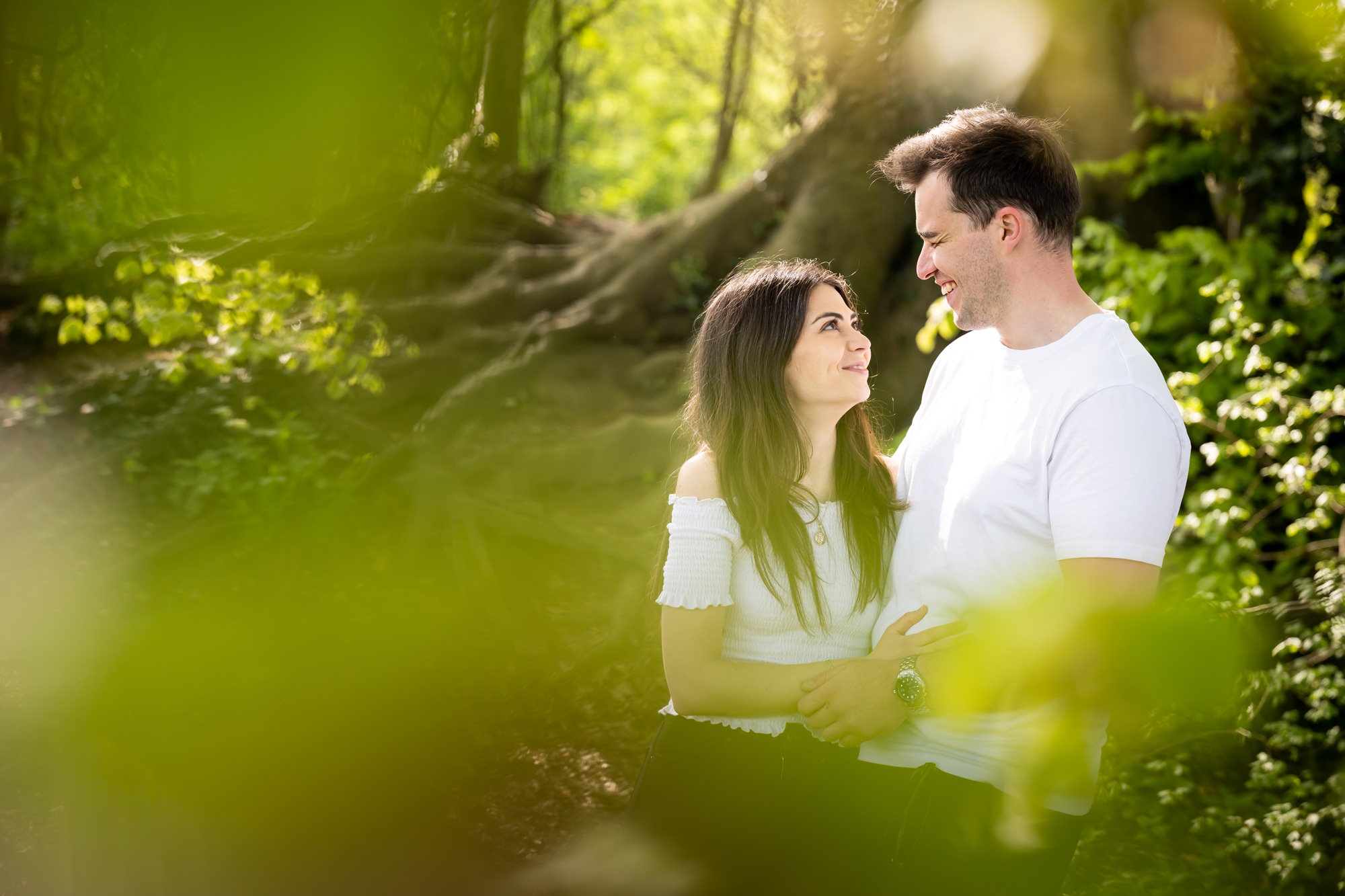Bride and groom behind green leaves look at each other and smile in Verulamium Park St Albans