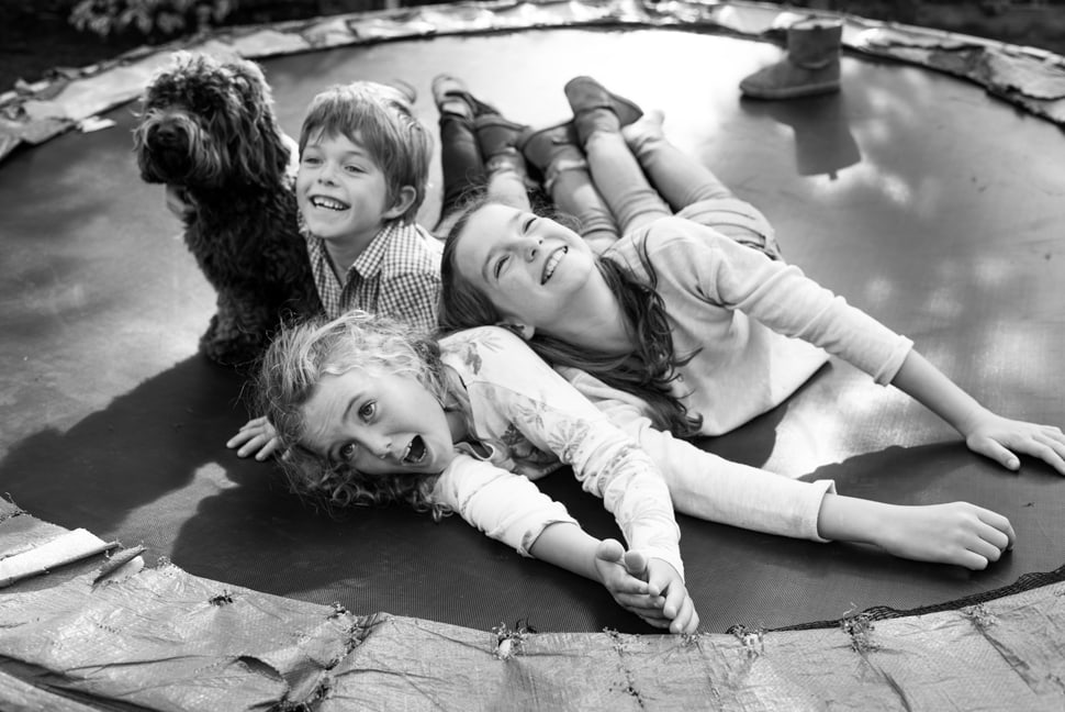 three siblings and family dog laughing on the trampoline