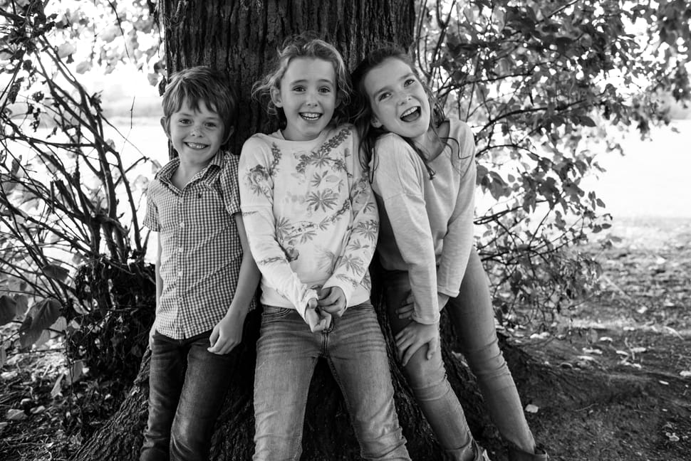 siblings laughing leaning against a tree during family photoshoot