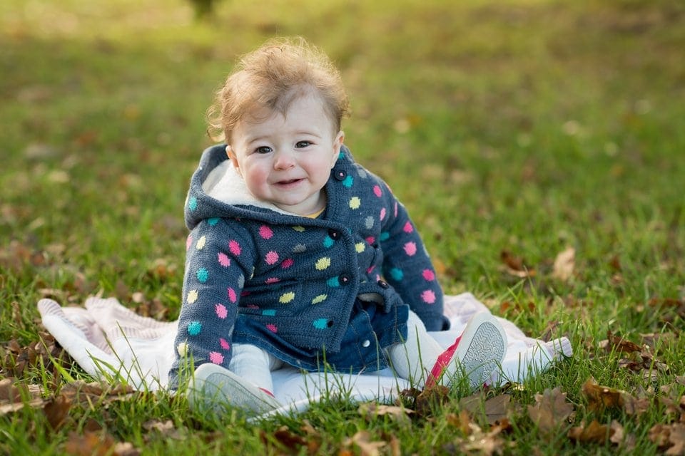 smiling baby girl sitting on a rug in the park