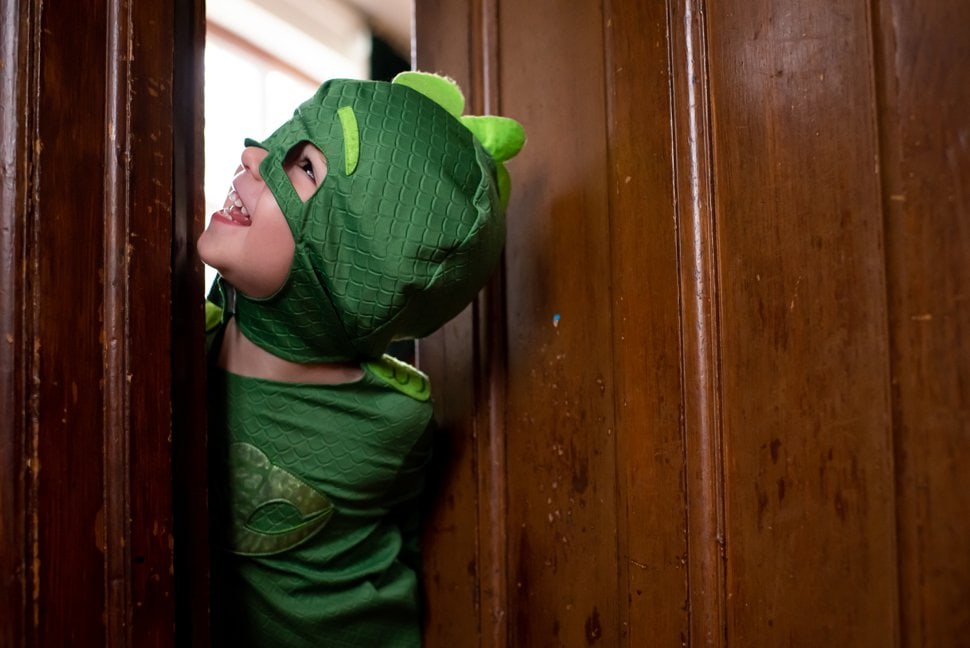 kid in superhero costume peering round door