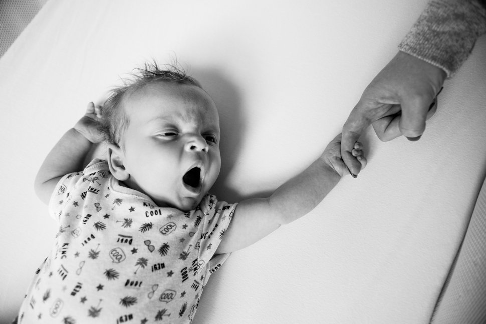 yawning baby holds mums finger during family photoshoot