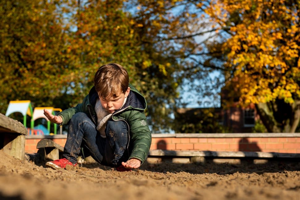 little boy playing in a sandpit during autumnal family photoshoot