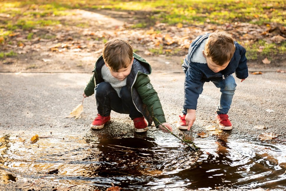 brothers playing with sticks in a muddy puddle