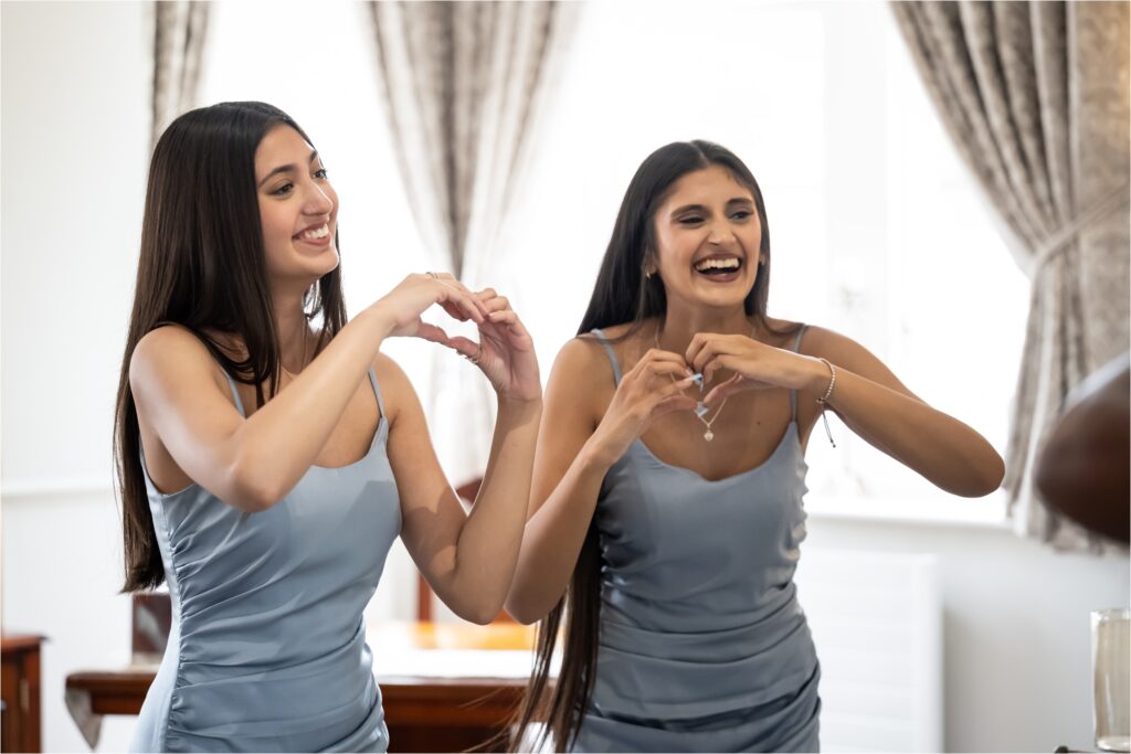 Bridesmaids make heart shapes with hands and dance waiting for wedding ceremony
