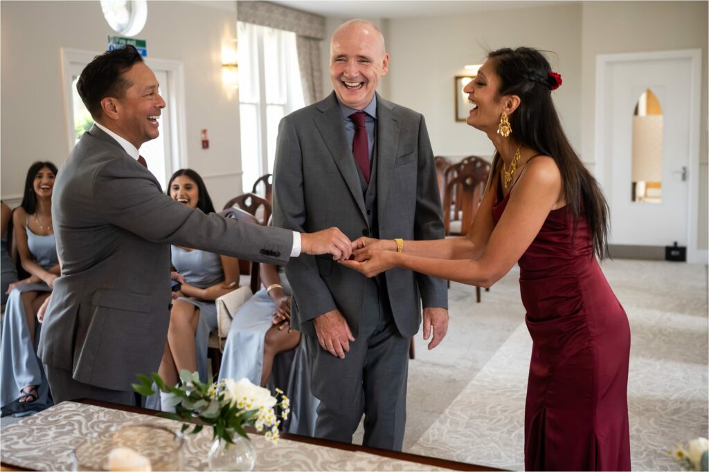 Bride and groom laugh as best man hands over ring during wedding ceremony