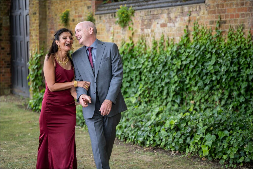 Bride and groom laugh walking through gardens with linked arms