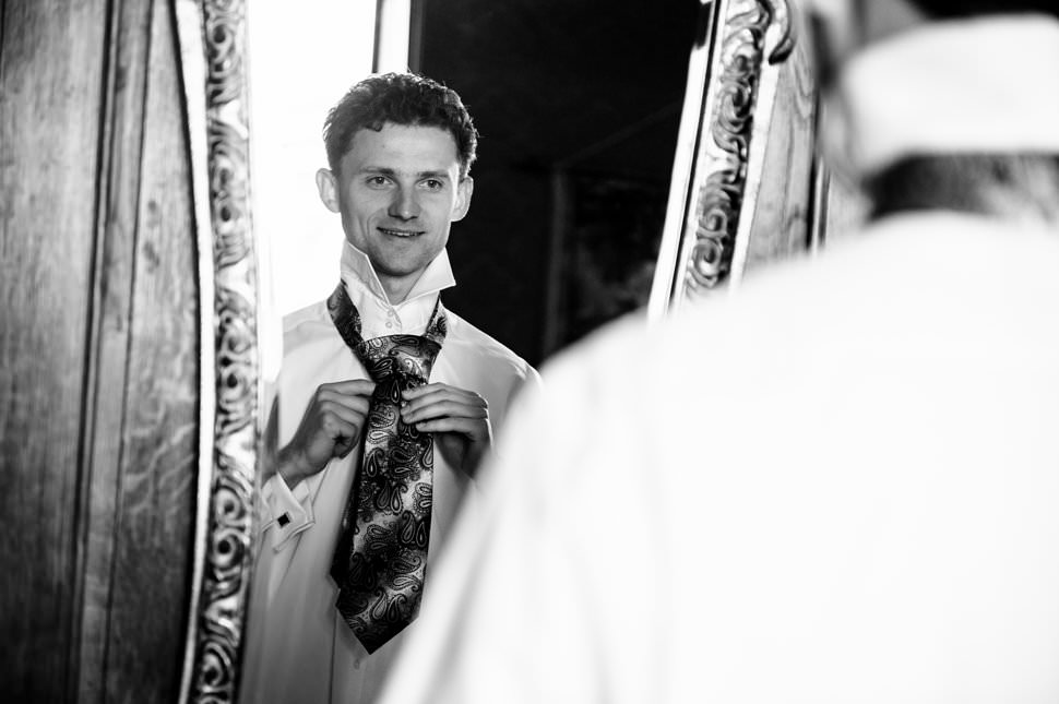 groom putting on tie in mirror