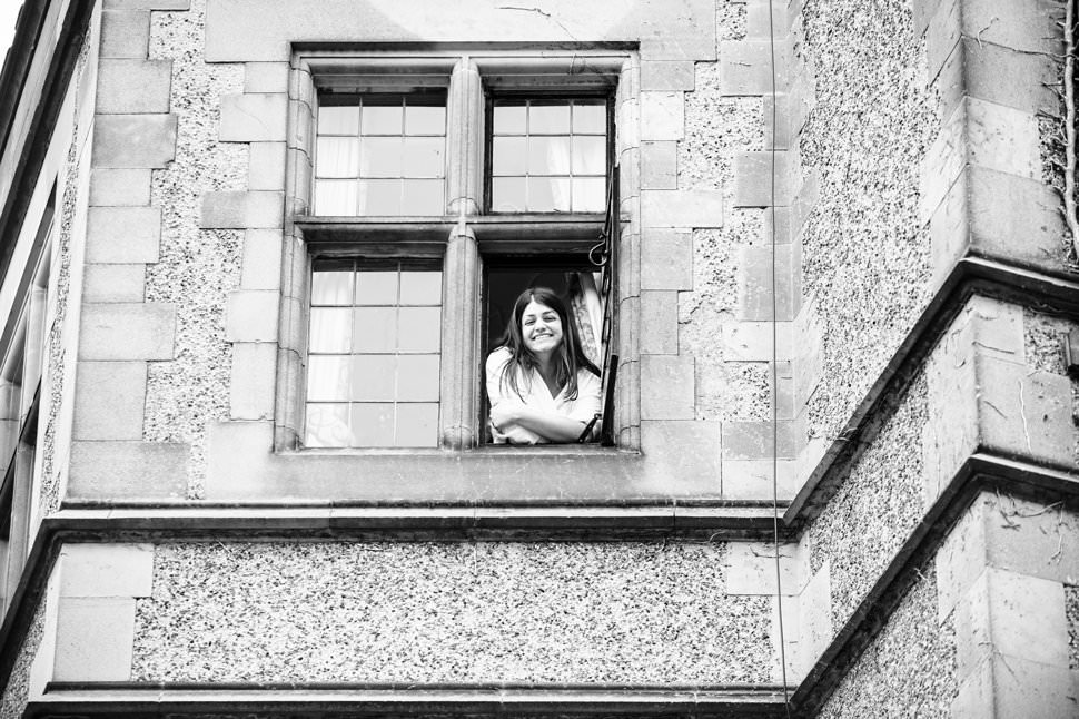 A happy bride leans out of a Fanhams Hall window while getting ready for her wedding.