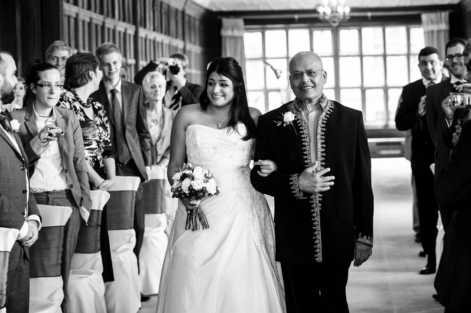 A proud father escorts a happy bride down the aisle in the Long Gallery at a Fanhams Hall wedding.