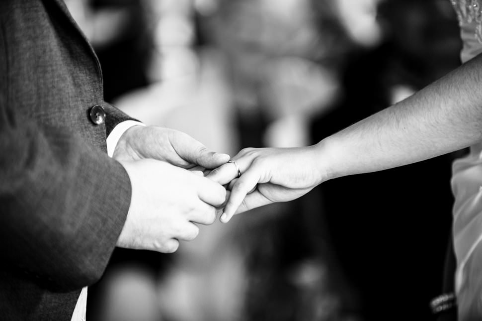 A close up of a groom putting a ring onto a brides finger during a wedding ceremony.