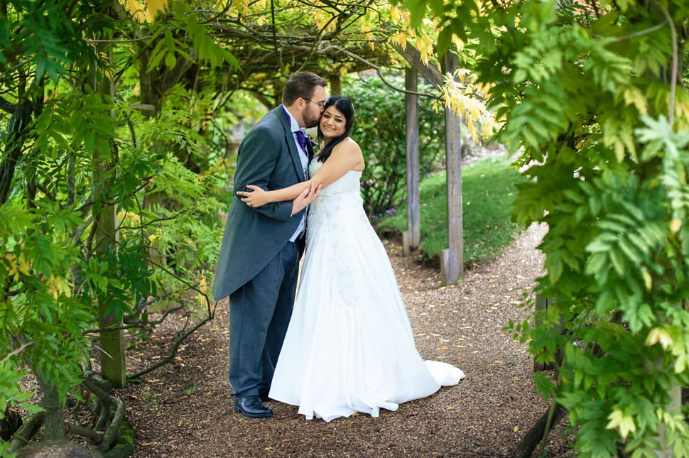 A bride and groom cuddle in a leafy tree tunnel.