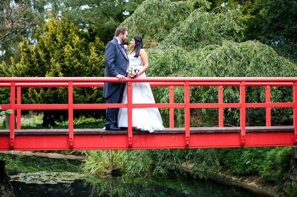 A bride and groom stand on a red Japanese bridge at Fanhams Hall