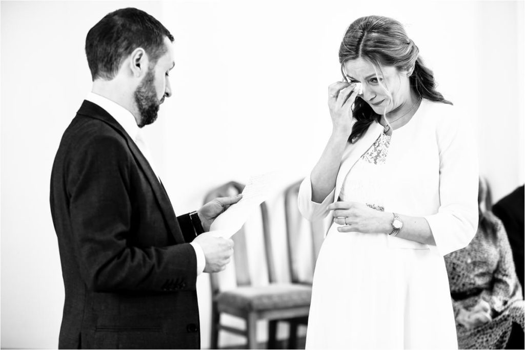 Bride wipes away a tear while groom reads handwritten vows at St Albans Registry Office wedding.