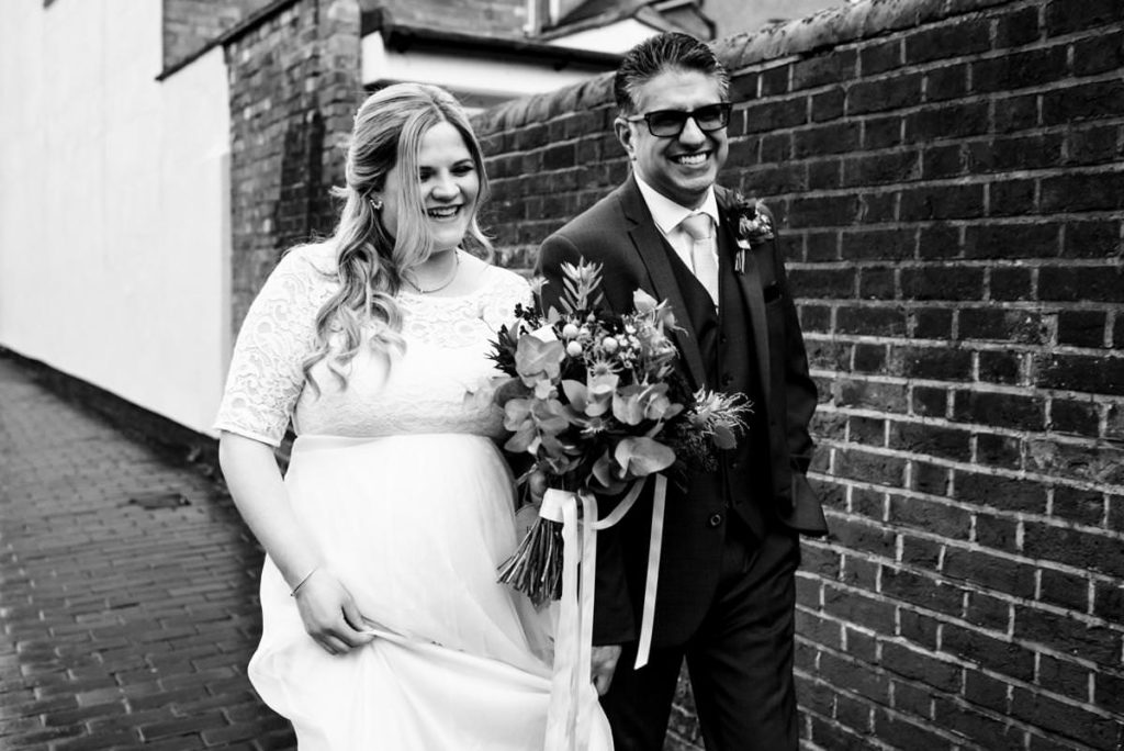 A laughing bride and groom walk through the streets of St Albans after their wedding.