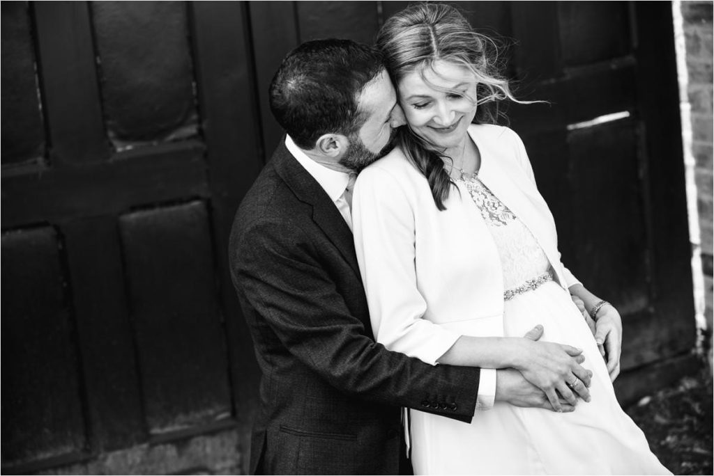 Groom cuddles pregnant wife after St Albans Registry Office wedding.