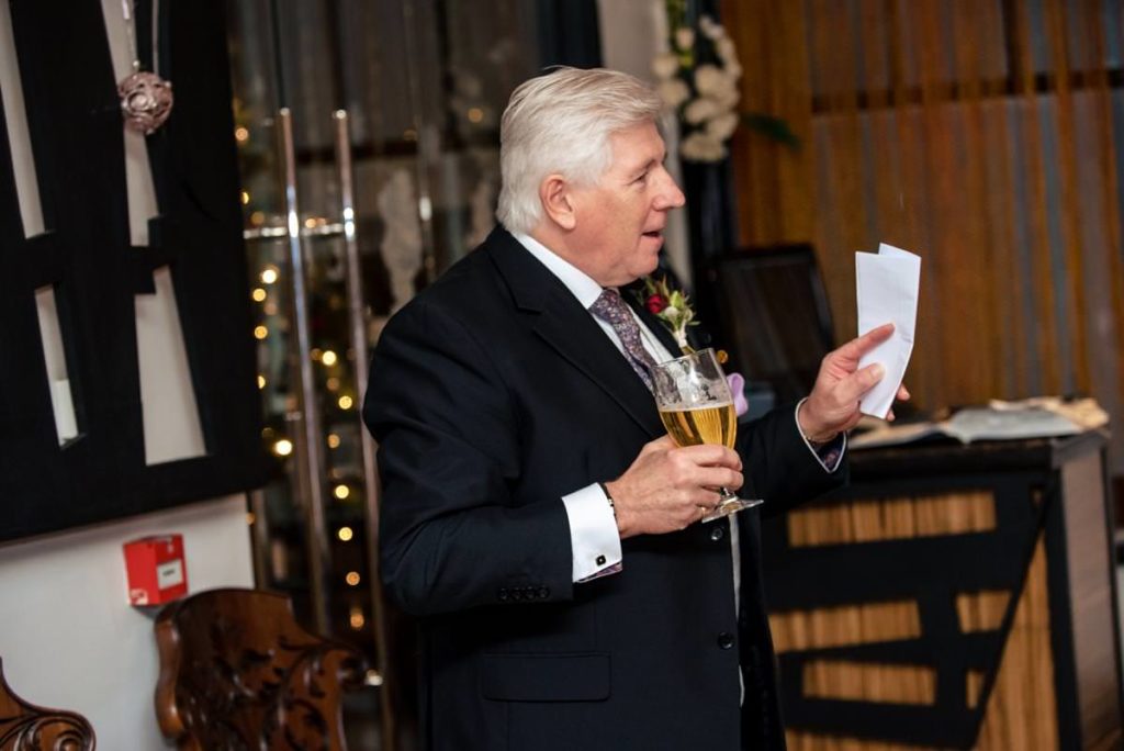 A father of the bride gives a wedding speech while holding a beer and his notes.