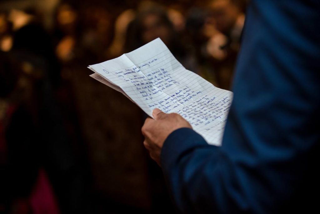Groom holds his hand written wedding speech while wearing blue suit.