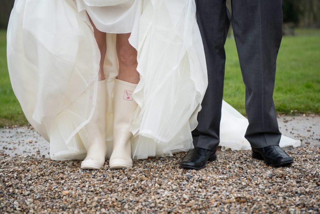 Bride wearing wellies shows shoes at a wet wedding