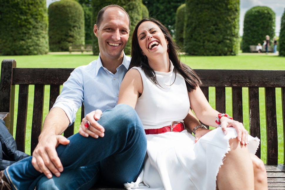 Couple sitting on park bench laughing into camera
