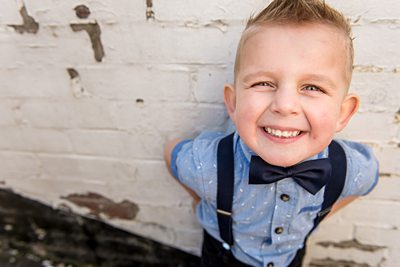Little boy in bow tie grins up at camera during family photo shoot
