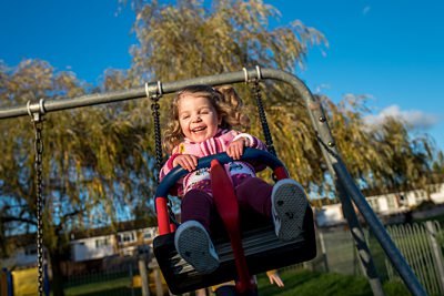 Girl laughs while being pushed high on a swing in St Albans