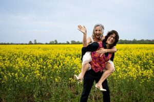 Laughing bride carrying wife on her back in front of yellow field