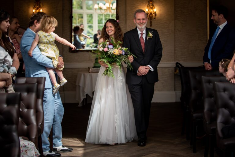 Bride smiles at child while being walked down aisle by father