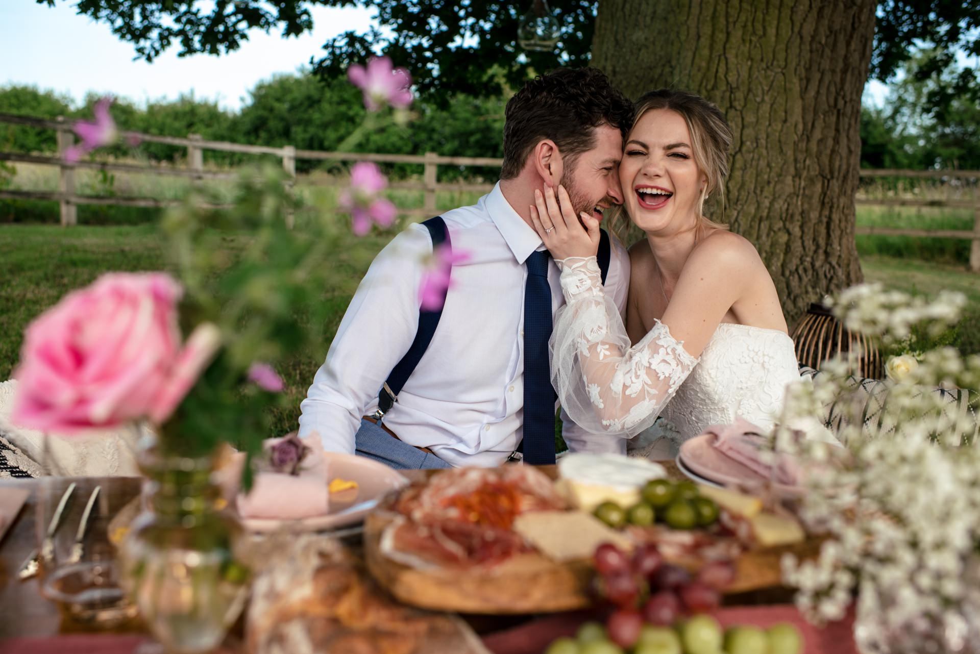 Bride and groom laugh during intimate low table couple picnic at Milling Barn in Hertfordshire