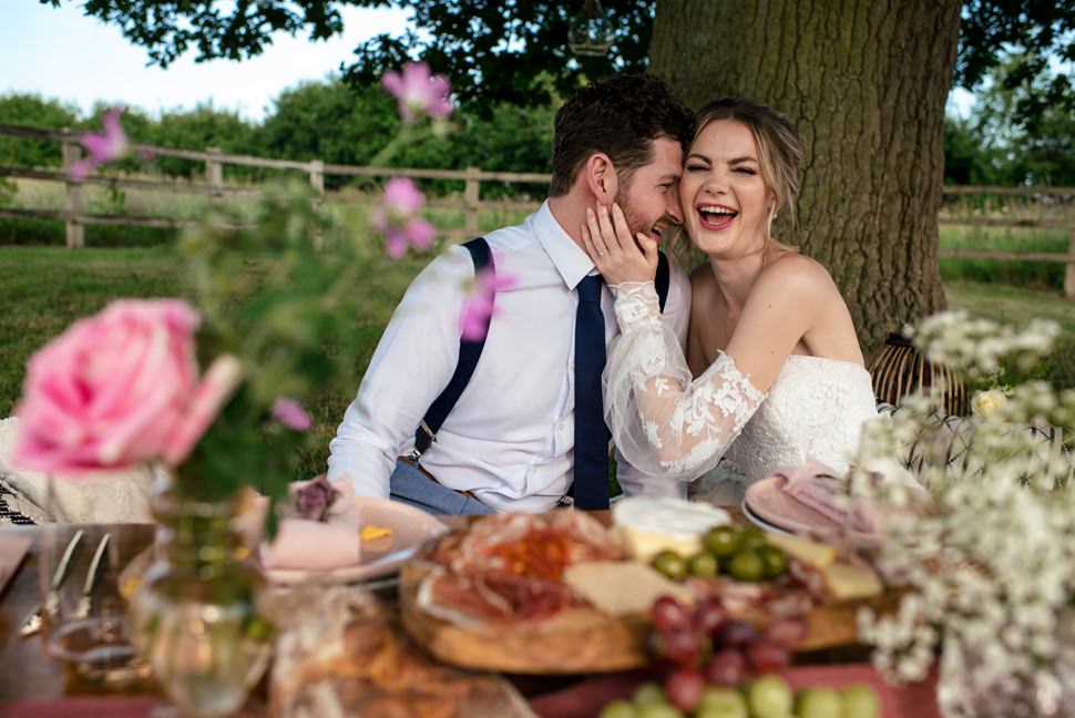 Bride and groom laugh at low picnic table