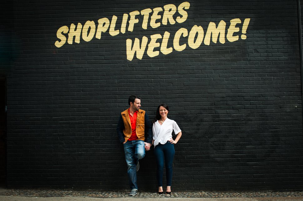 Couple hold hands in front of shoplifters welcome graffiti