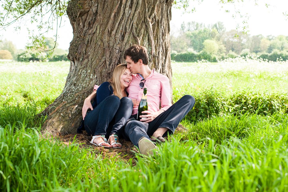 Groom kisses bride on head while sitting on tree trunk holding champagne