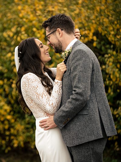 Bride and groom embrace at autumn wedding in front of yellow trees at Coltsfoot
