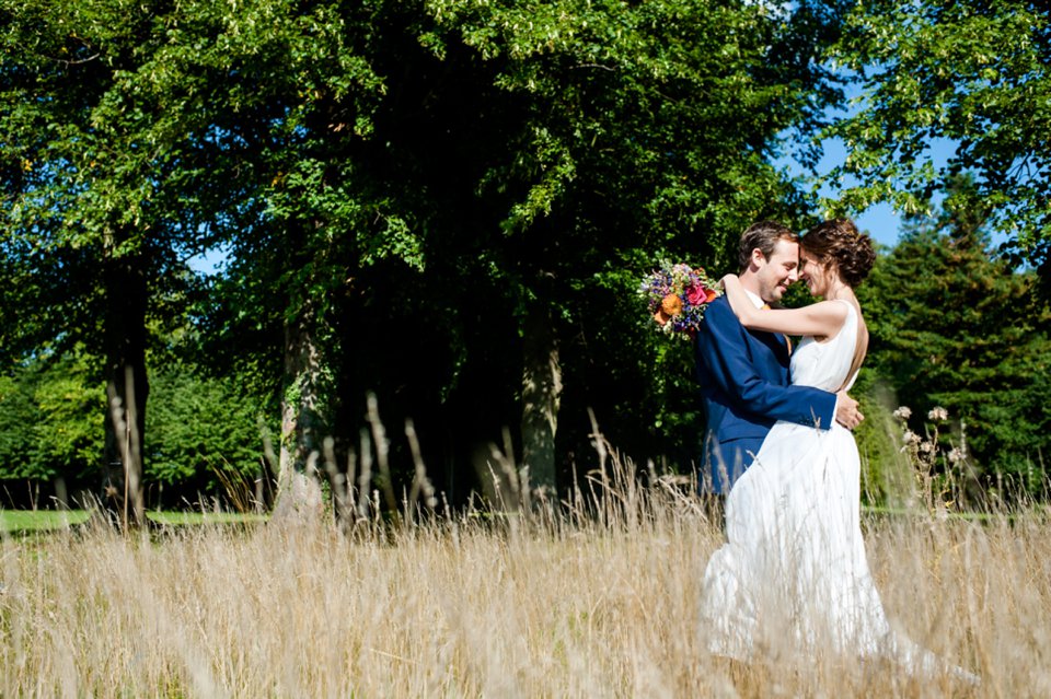Bride and groom hug in long grass on bright sunny day