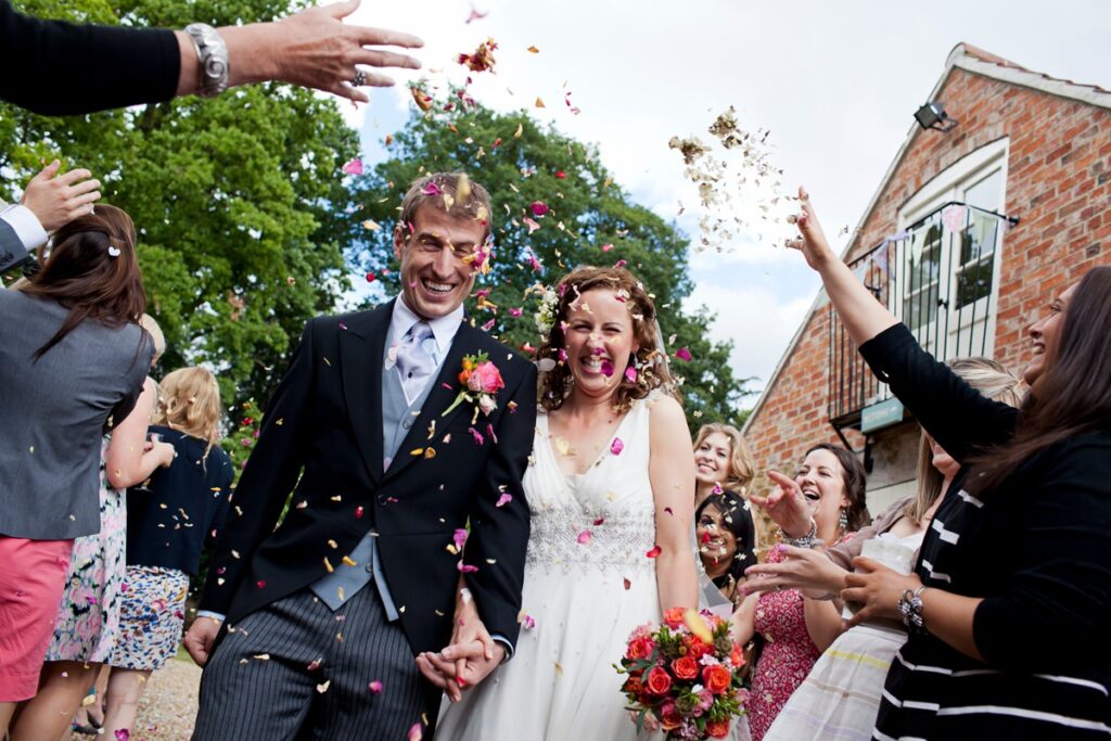 Bride and groom laugh in fresh petal confetti toss at Hertfordshire wedding