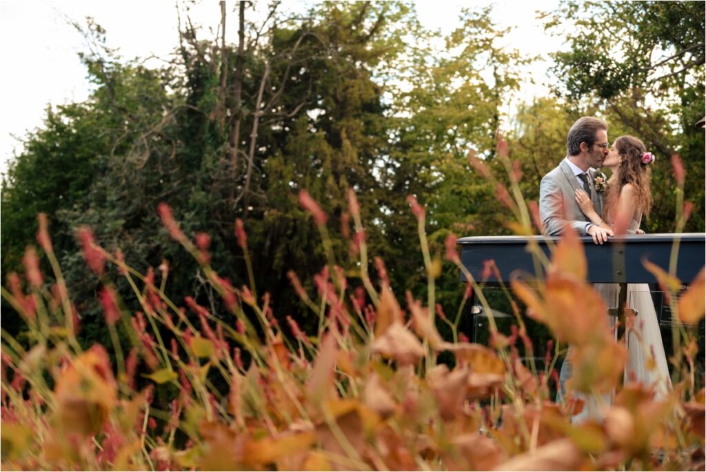 Bride and groom kiss on pier behind autumnal leaves at St Michael's Manor Hotel at Hertfordshire wedding