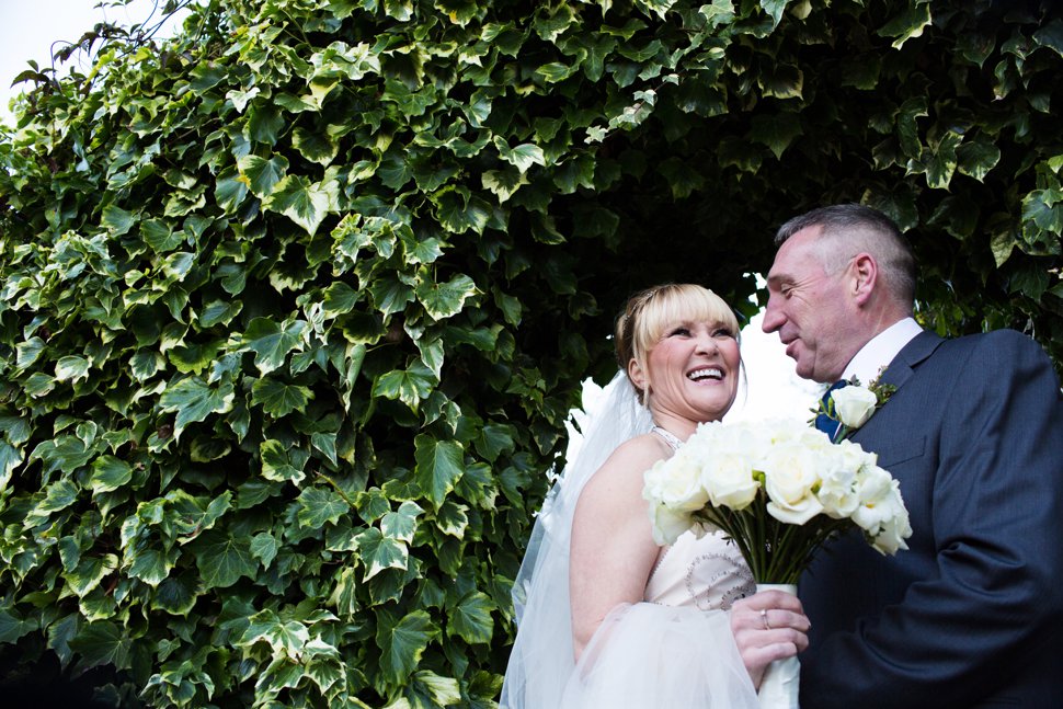 Bride and groom laugh in ivy arch