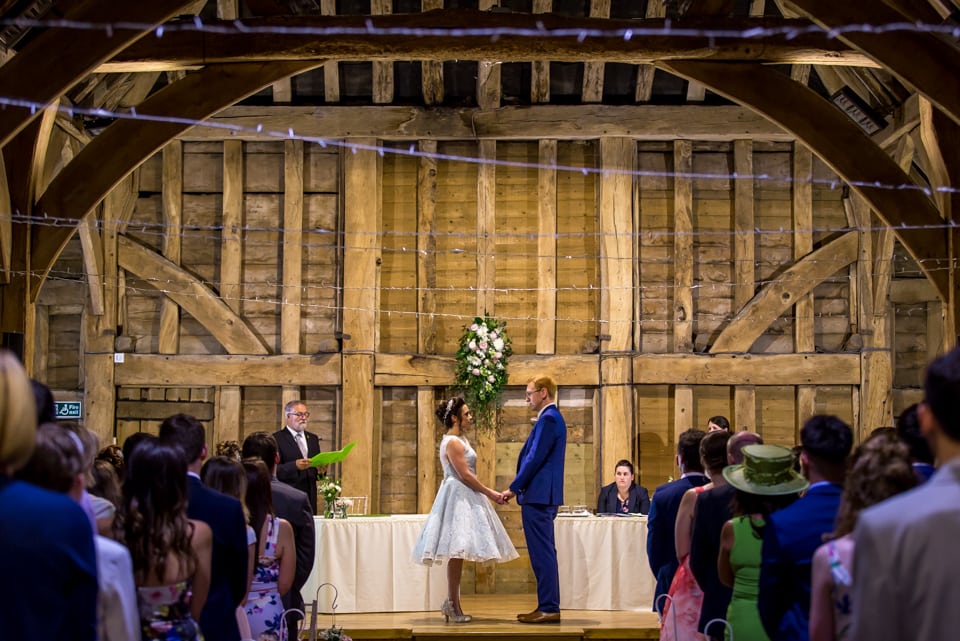 Bride wearing short blue wedding dress holds hands with groom in blue suit at priory barn in hertfordshire