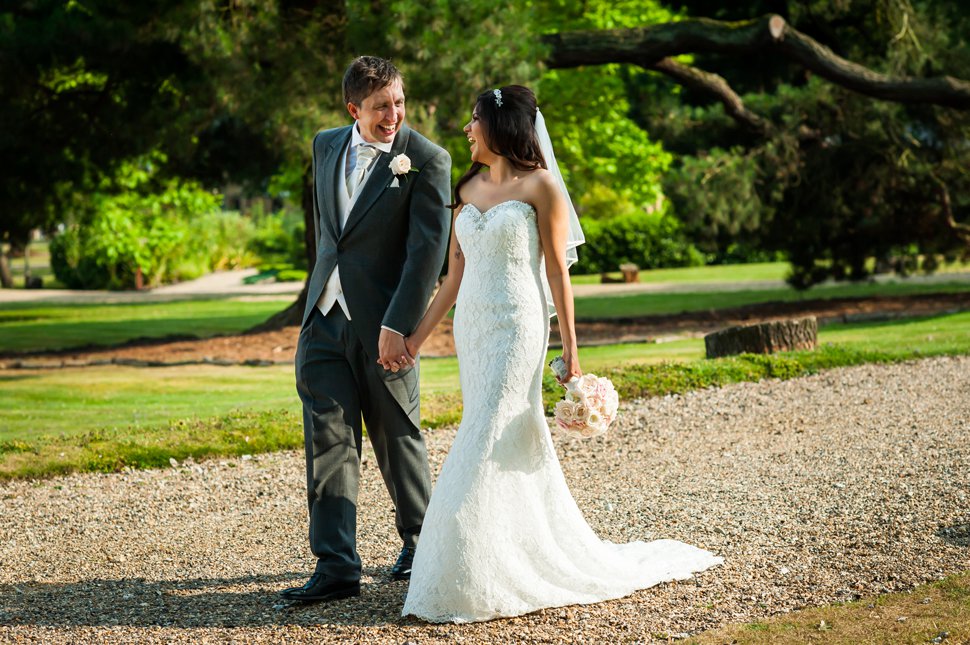 Laughing bride and groom walk through green gardens smiling at each other at Hertfordshire wedding