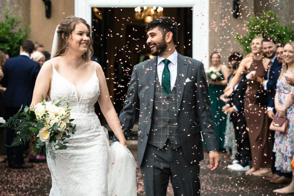 Smiling couple walk through confetti lines at Offley Place wedding in Hertfordshire