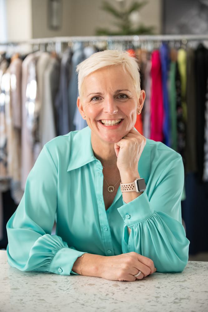 smiling personal stylist in turquoise shirt in front of rail of clothes during personal branding shoot