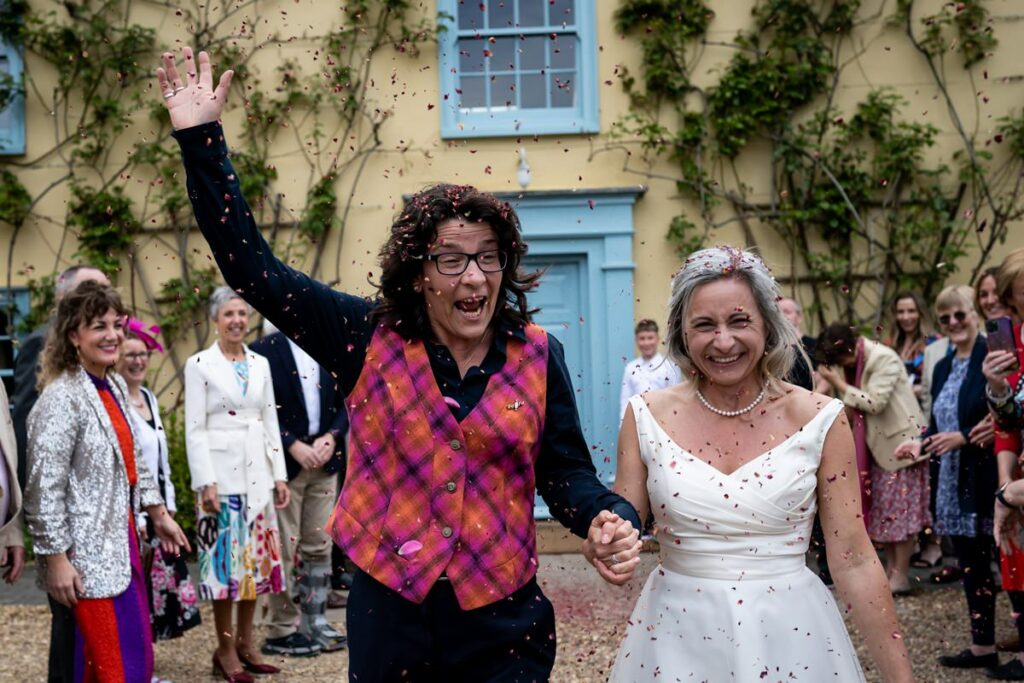 Two happy brides enjoy south Farm confetti throw in front of farm house