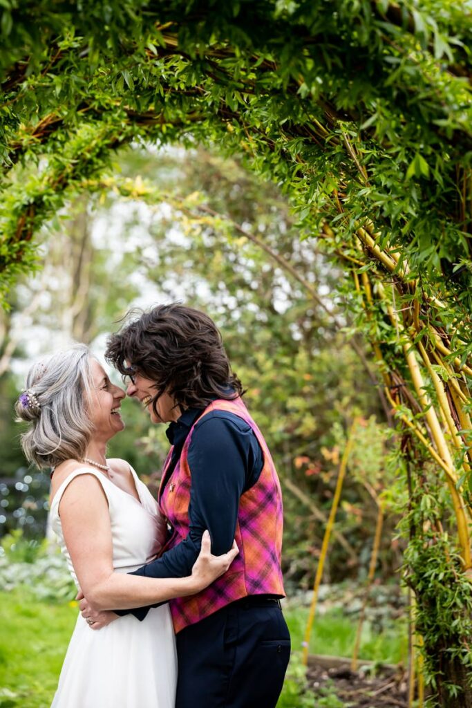 Two brides laugh under willow arch at South Farm wedding