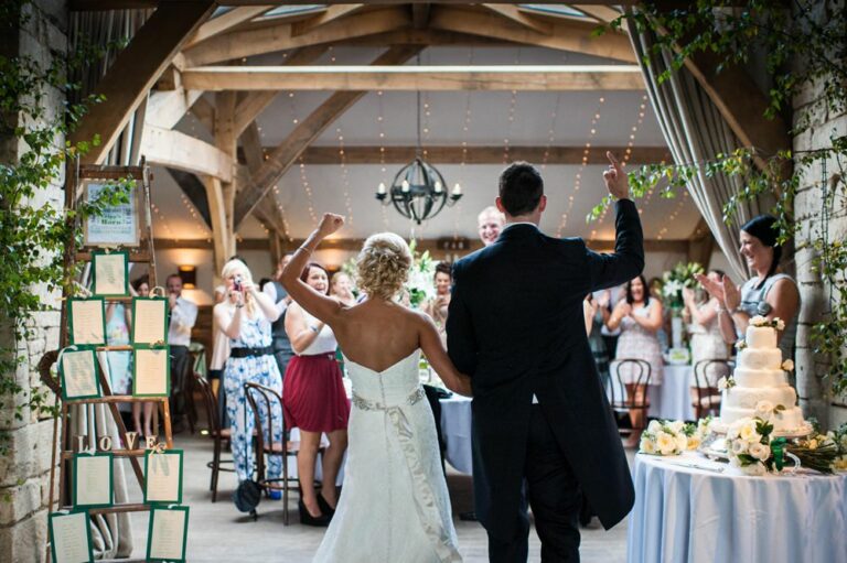 Bride and groom cheer while entering wedding breakfast at Cripps Barn