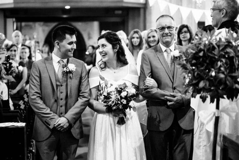 Bride beams at groom at top of church aisle at Hertfordshire wedding