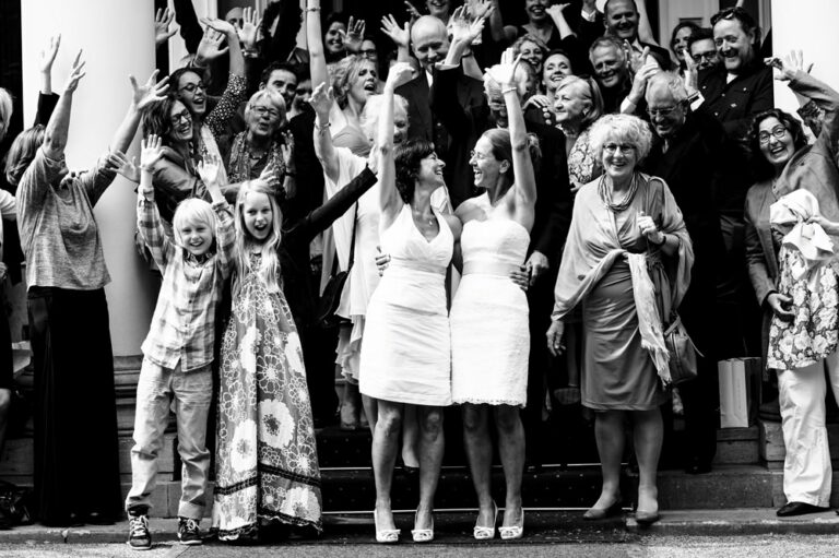 Two brides cheer with friends and family during group shot