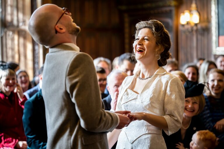 Bride and groom laugh during ring exchange in wedding ceremony at Rothamsted Manor