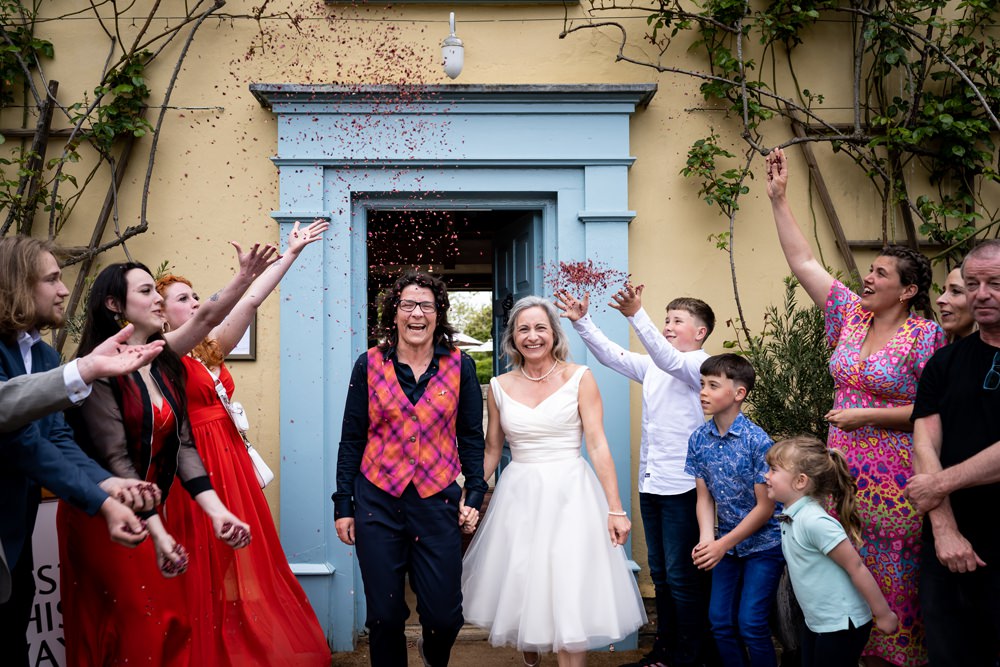 Two brides walk under confetti throw at South Farm wedding