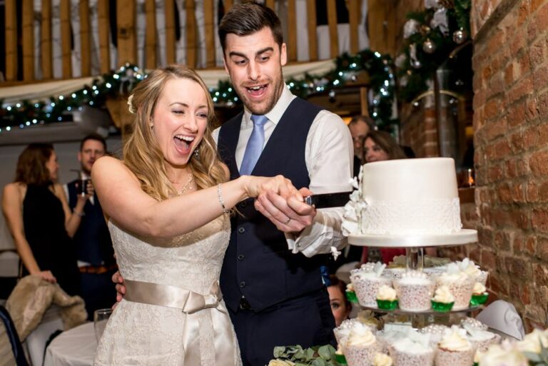 Laughing bride and groom cut wedding cake at Tewinbury Farm