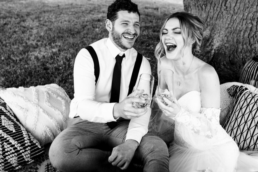 Bride and groom laugh with champagne at Milling Barn